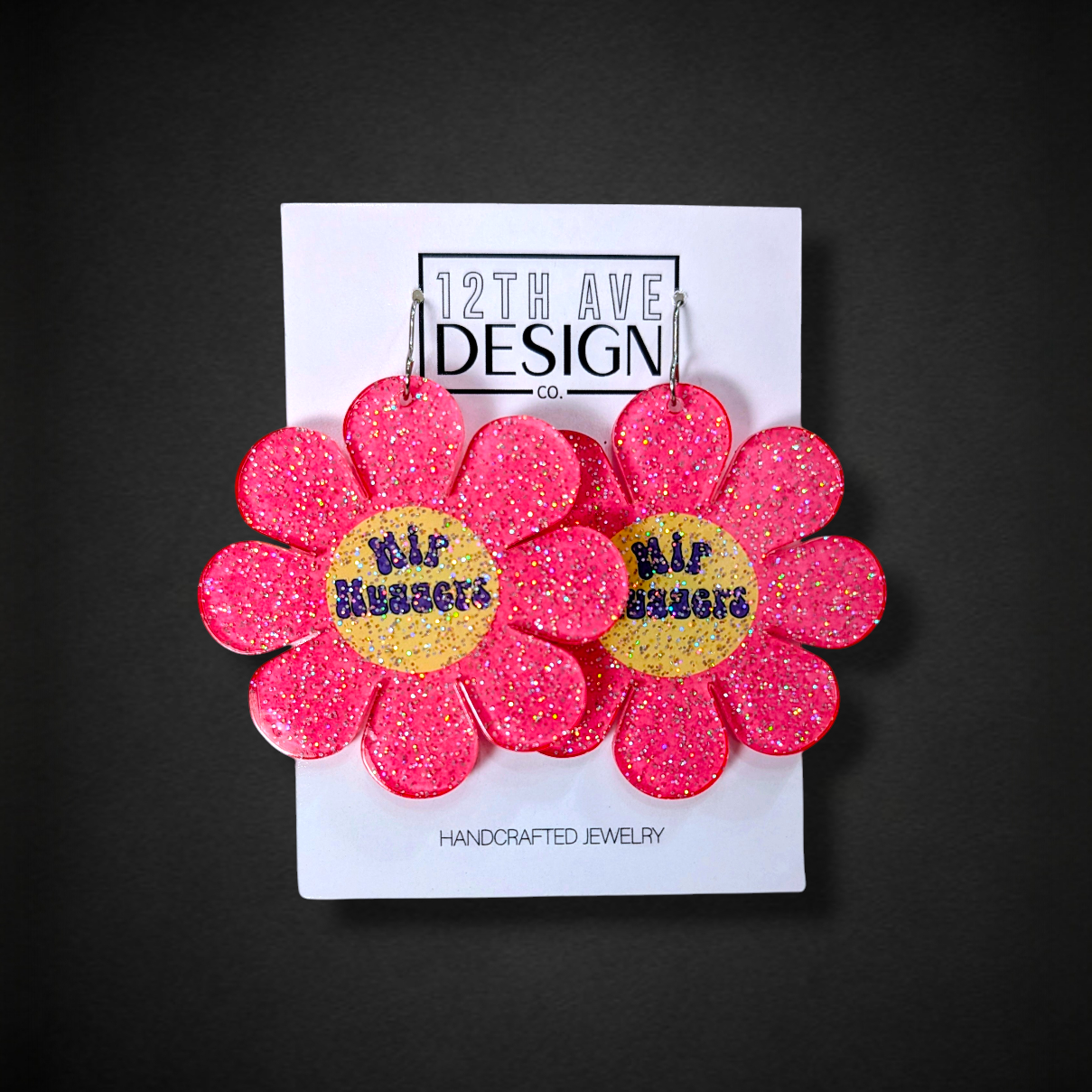 Pink flower-shaped earrings on a 12th Ave Design card against a black background