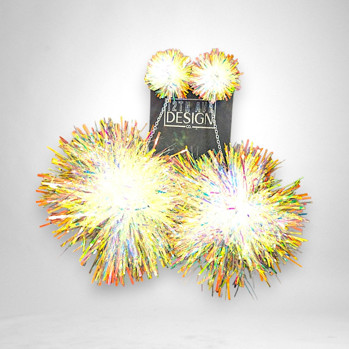 12th Ave Design Co. iridescent tinsel pompom earrings with silver chains and peace sign charms on display card