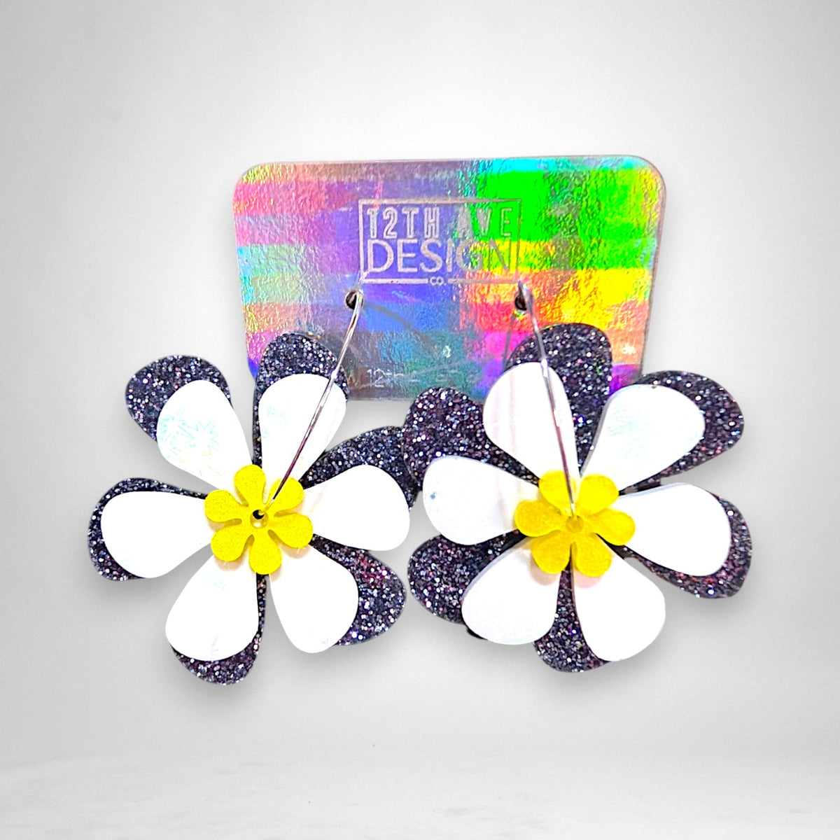12th Ave Design Co. acrylic daisy hoop earrings with white and glittery black petals on stainless steel hoops.