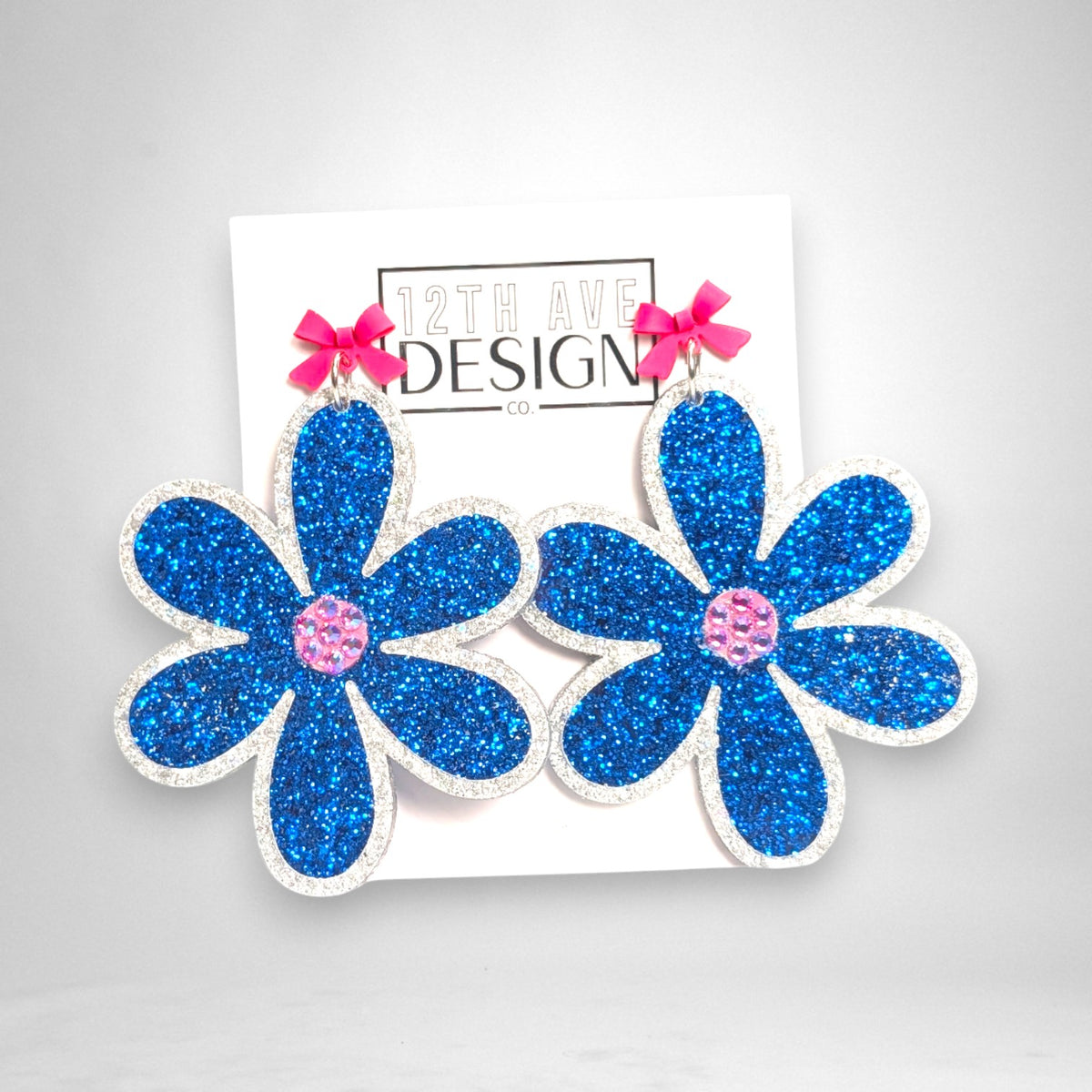 12th Ave Design Co. statement floral earrings with blue glitter acrylic petals, pink crystal centers, and bow studs.