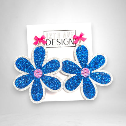 12th Ave Design Co. statement floral earrings with blue glitter acrylic petals, pink crystal centers, and bow studs.