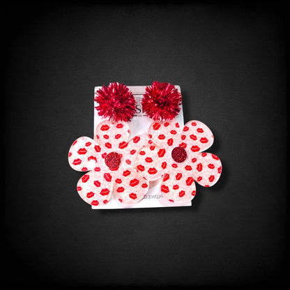 12th Ave Design Co. Bubble Daisy earrings featuring a pink lip print, red glitter centers, and red pom-pom accents.