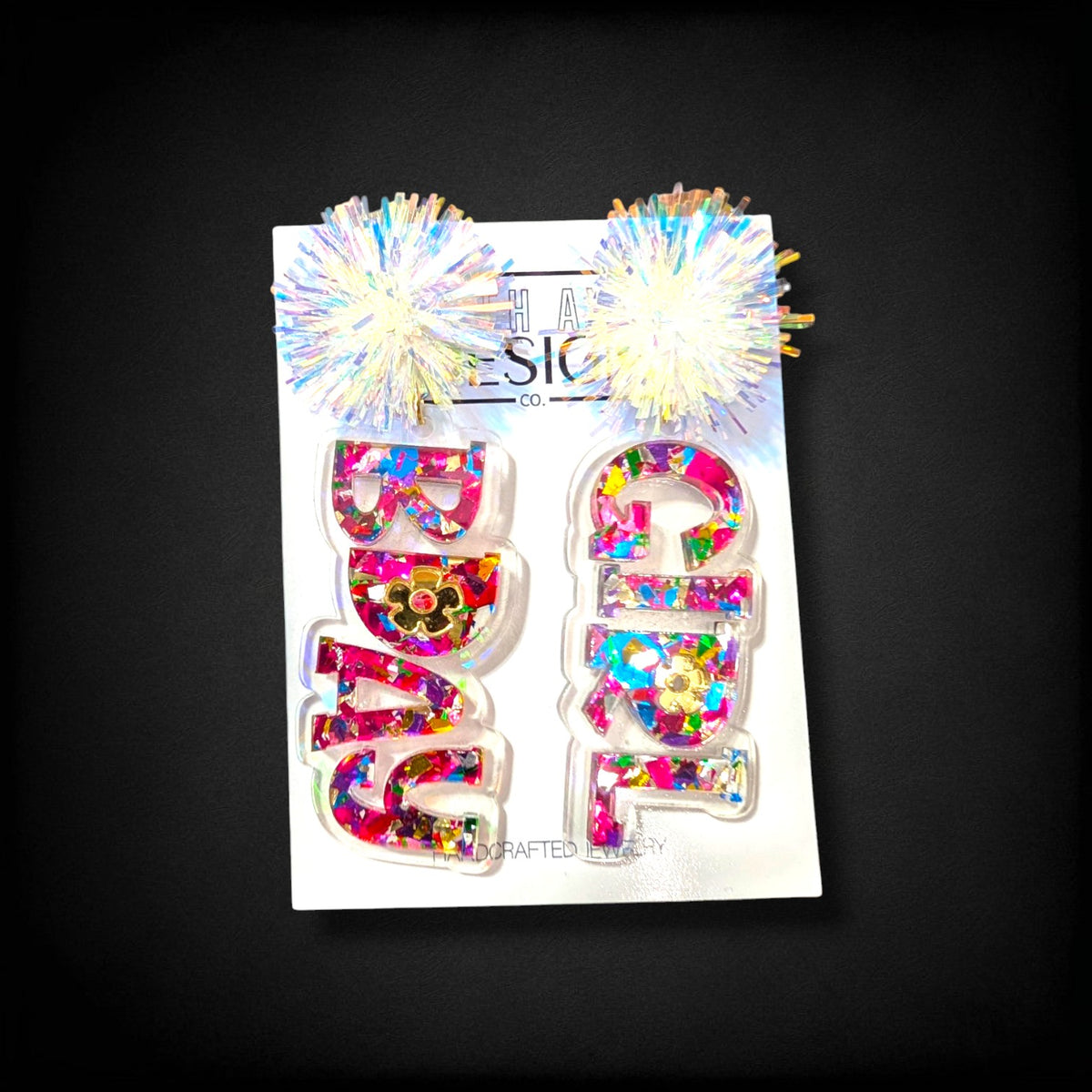 12th Ave Design Co. custom acrylic Bad Girl earrings featuring iridescent pom-poms and colorful confetti glitter.