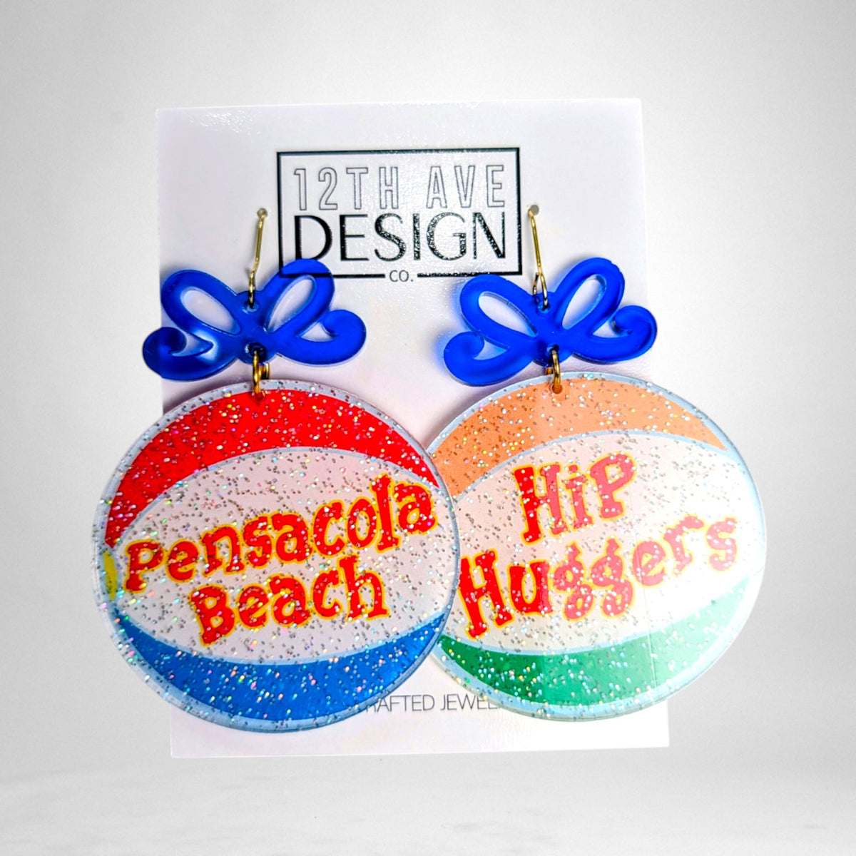 12th Ave Design Co. custom glitter acrylic earrings featuring Pensacola Beach and Hip Huggers text with blue bows.