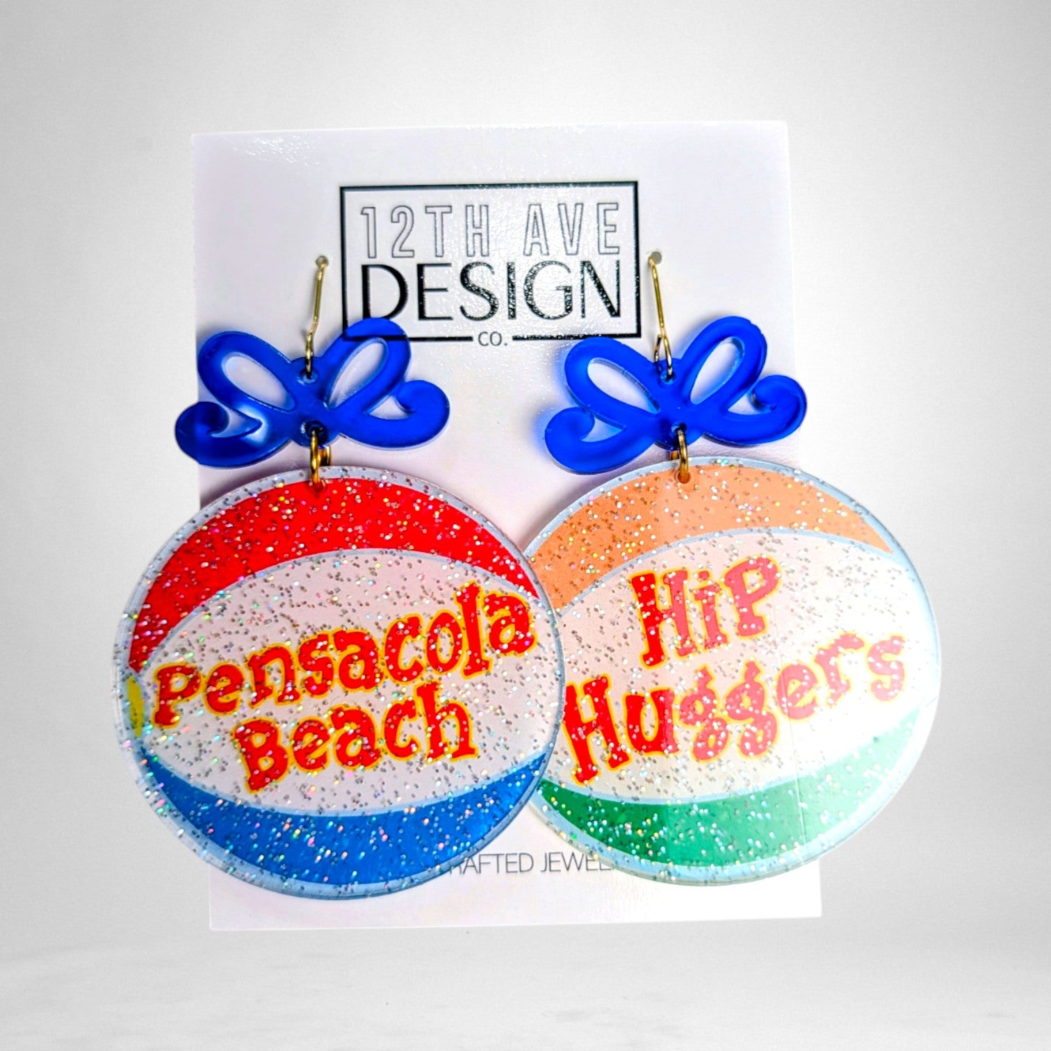 12th Ave Design Co. custom glitter acrylic earrings featuring Pensacola Beach and Hip Huggers text with blue bows.