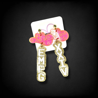 12th Ave Design Co. custom glittery pink cowboy hat earrings with white EMFC and XXIV lettering on a display card.
