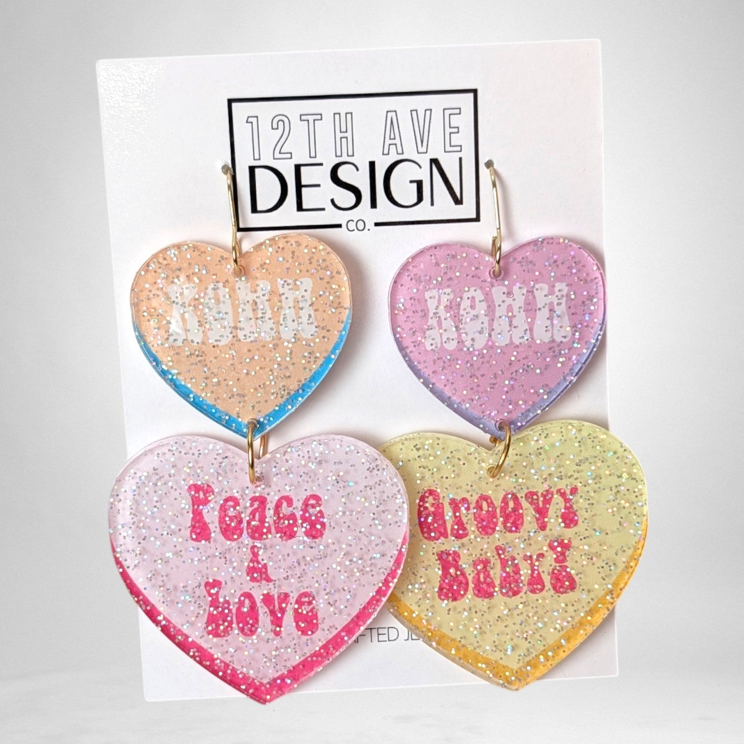 12th Ave Design Co. custom heart-shaped glitter acrylic earrings with KOHH, Peace & Love, and Groovy Baby text.