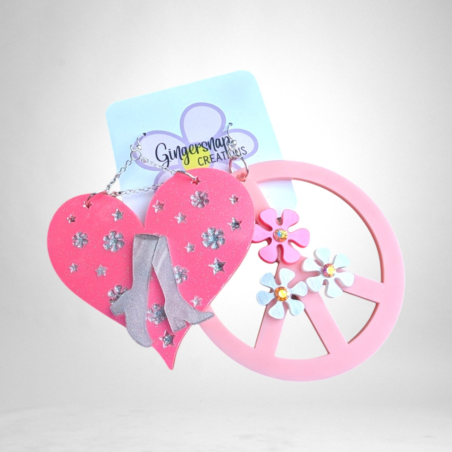 12th Ave Design Co. custom mismatched earrings featuring a pink glitter heart with boots and a pink peace sign charm.