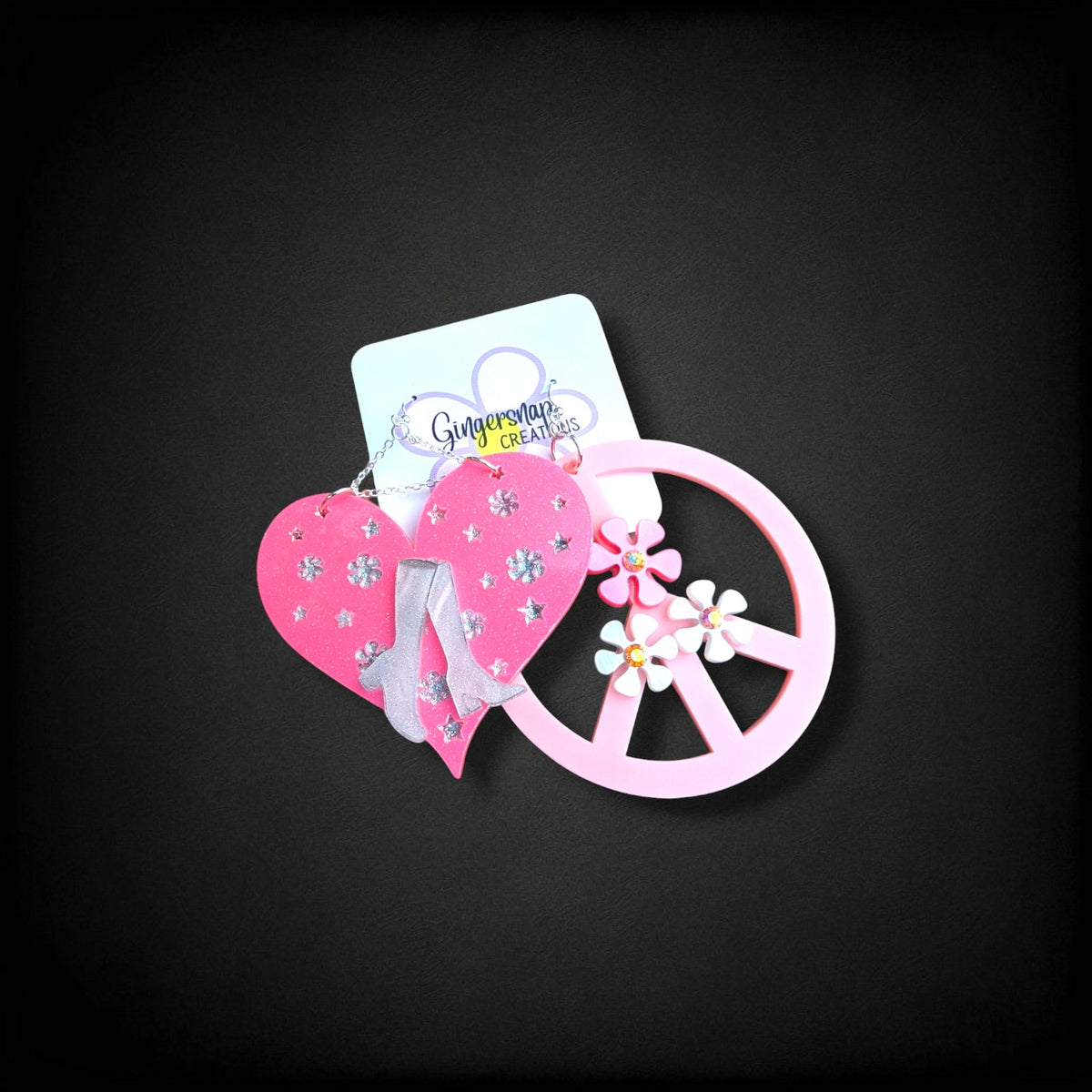 12th Ave Design Co. custom earrings featuring a pink glitter heart with silver boots and a pink peace sign charm.