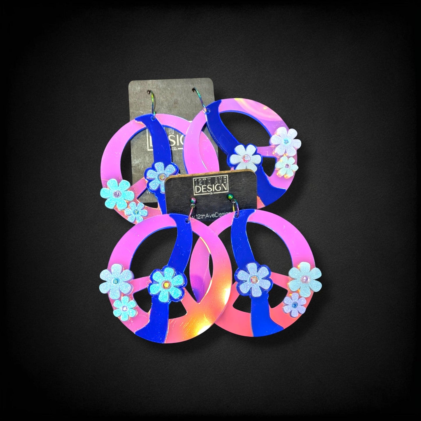 12th Ave Design Co. custom peace sign earrings featuring pink and blue acrylic with glittery flower accents.