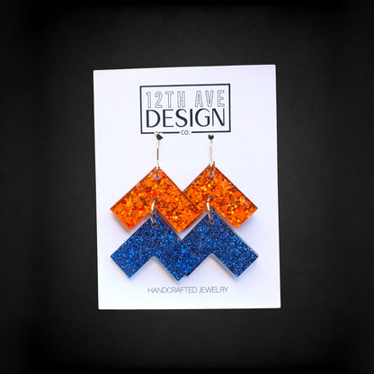 12th Ave Design Co. orange and blue glitter chevron drop earrings with surgical steel hooks on a display card