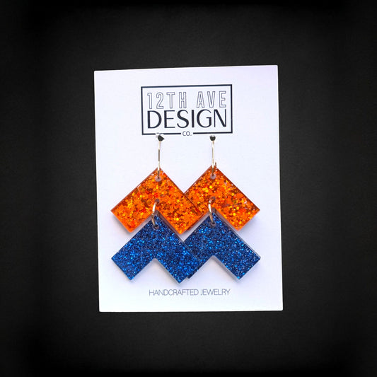 12th Ave Design Co. orange and blue glitter chevron drop earrings with surgical steel hooks on a display card