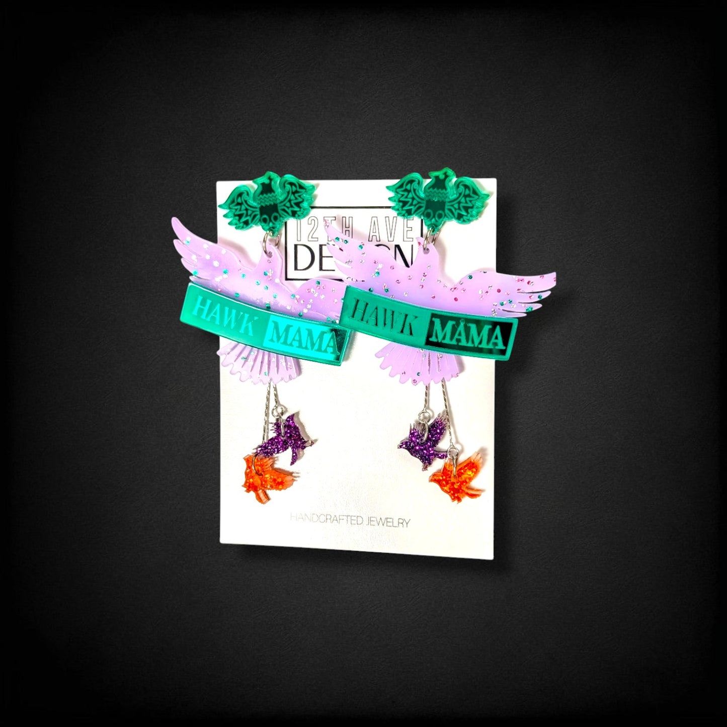12th Ave Design Co. custom Hawk Mama earrings featuring purple wings, green accents, and dangling bird charms.