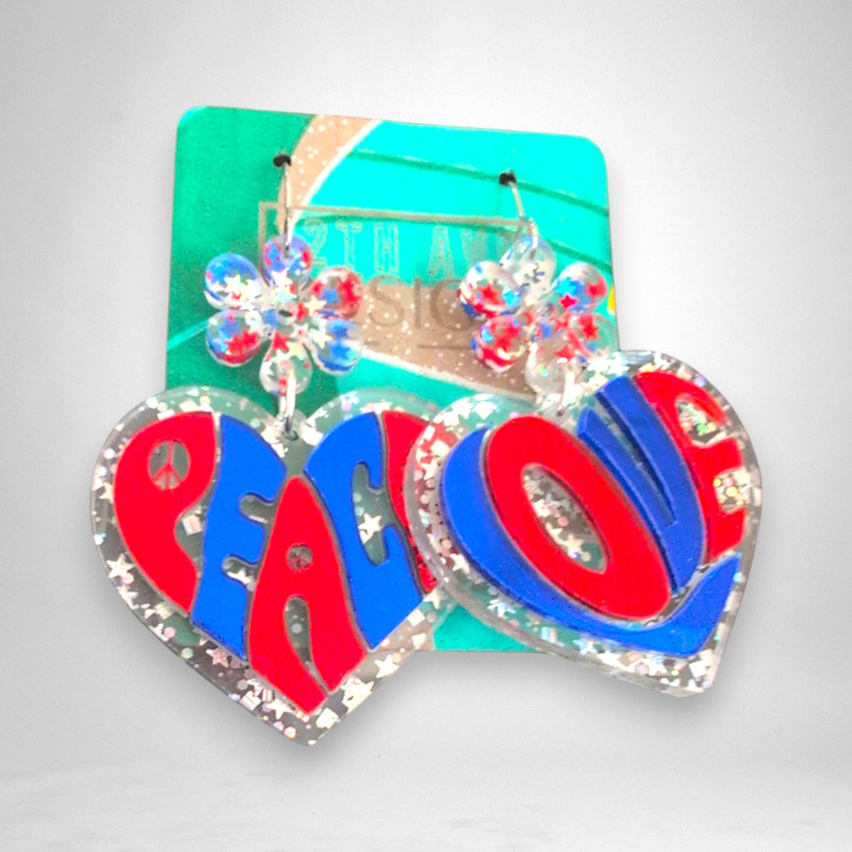 12th Ave Design Co. heart-shaped acrylic earrings with red and blue Peace and Love lettering and daisy accents.