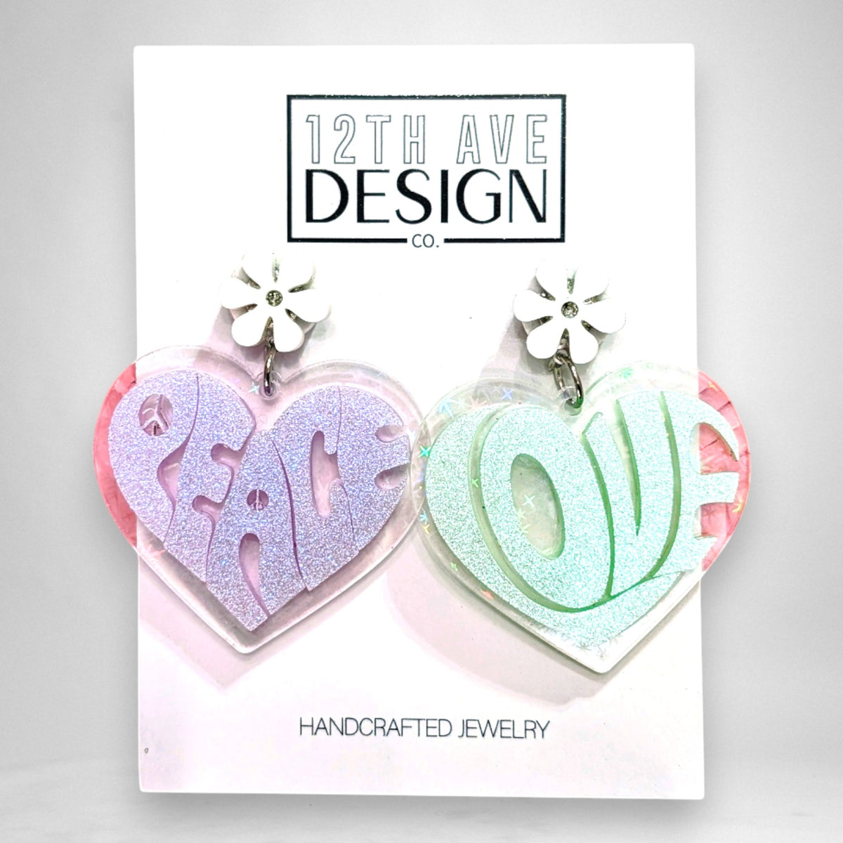 12th Ave Design Co. heart-shaped acrylic earrings with groovy Peace and Love lettering and white daisy accents.