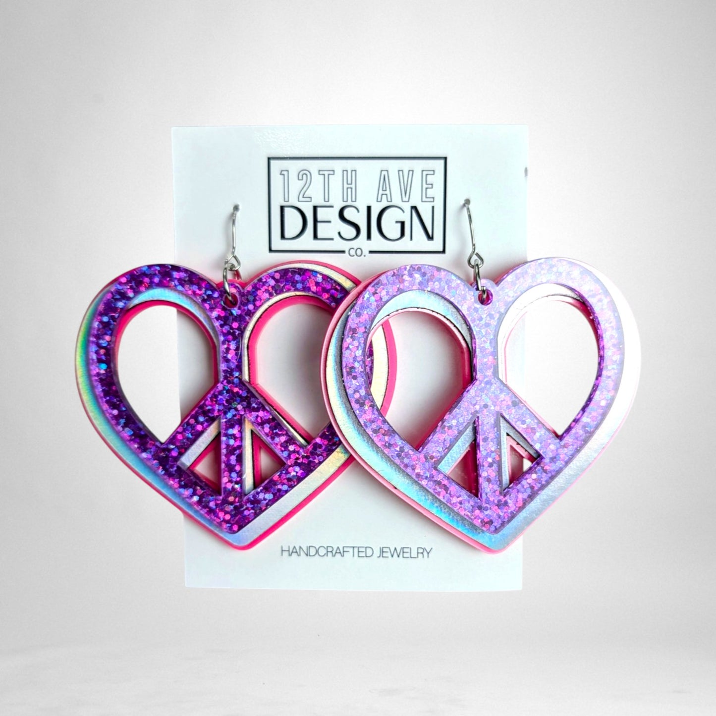 12th Ave Design Co. custom heart-shaped peace sign earrings featuring layered pink and purple glitter acrylic.