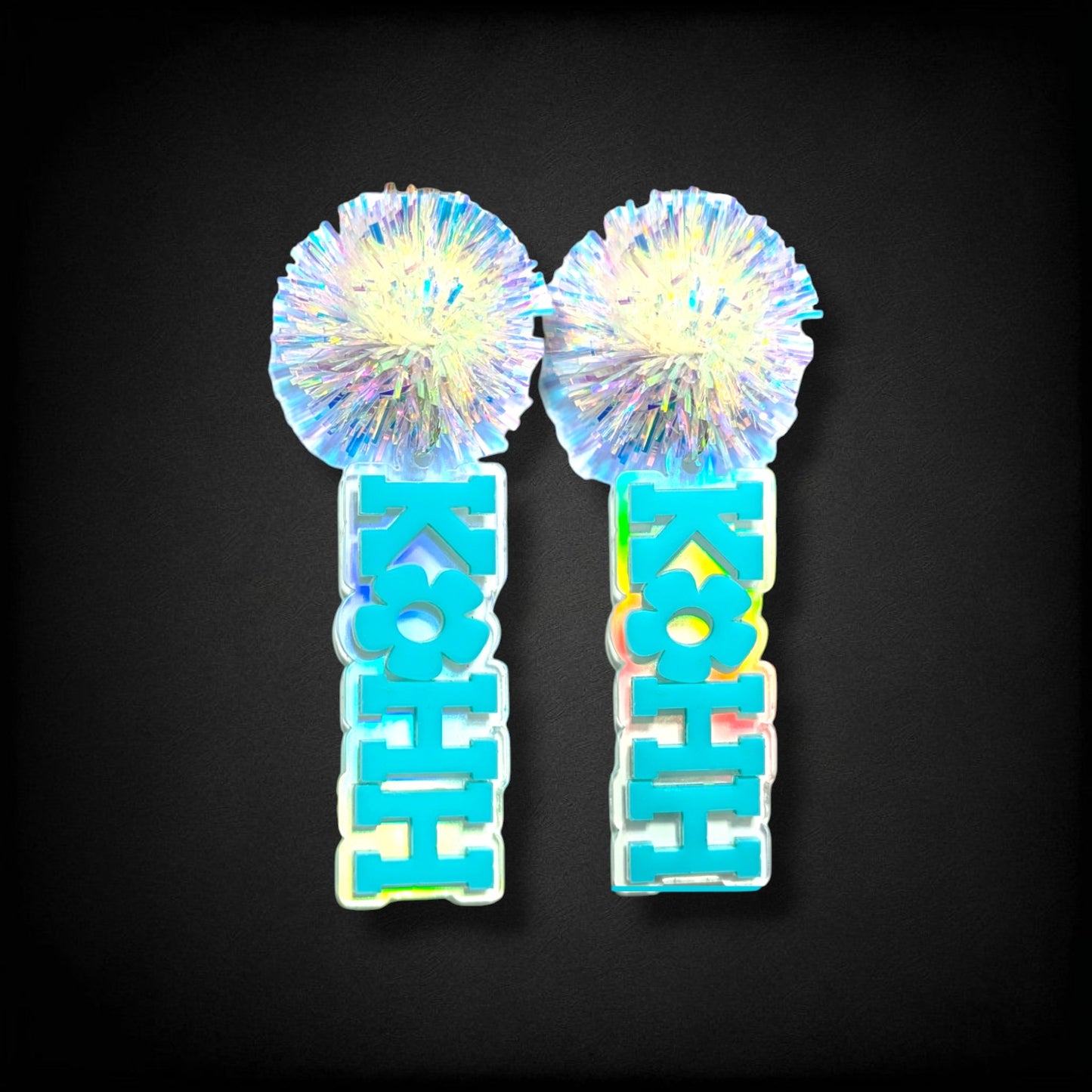 12th Ave Design Co. KOHH Varsity Bloom earrings featuring iridescent pom-poms and engraved blue acrylic lettering.