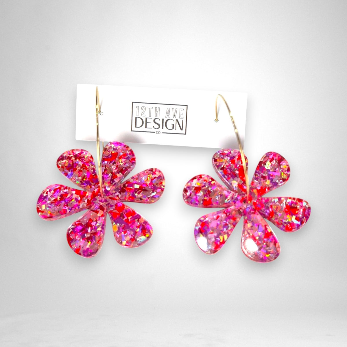 12th Ave Design Co. pink glitter acrylic daisy flower hoop earrings on a branded display card