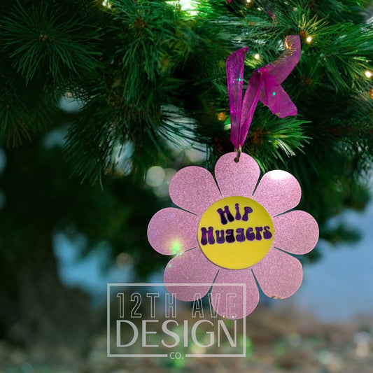 12th Ave Design Co. pink glitter flower holiday ornament with Hip Huggers text hanging on a Christmas tree