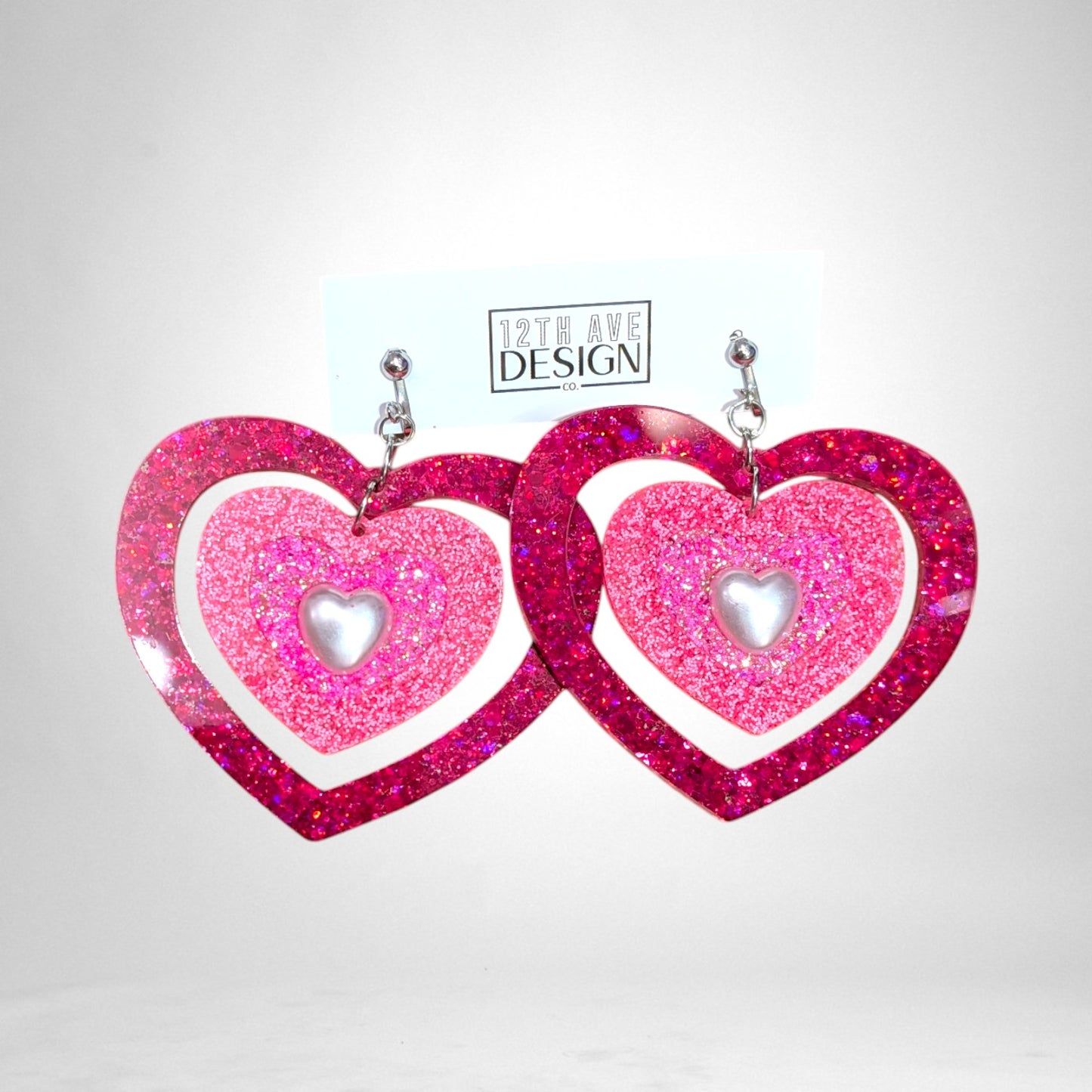 12th Ave Design Co. custom pink glitter heart earrings with layered resin frames and central pearl accents.
