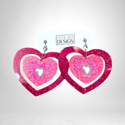 12th Ave Design Co. custom pink glitter heart earrings with layered resin frames and central pearl accents.