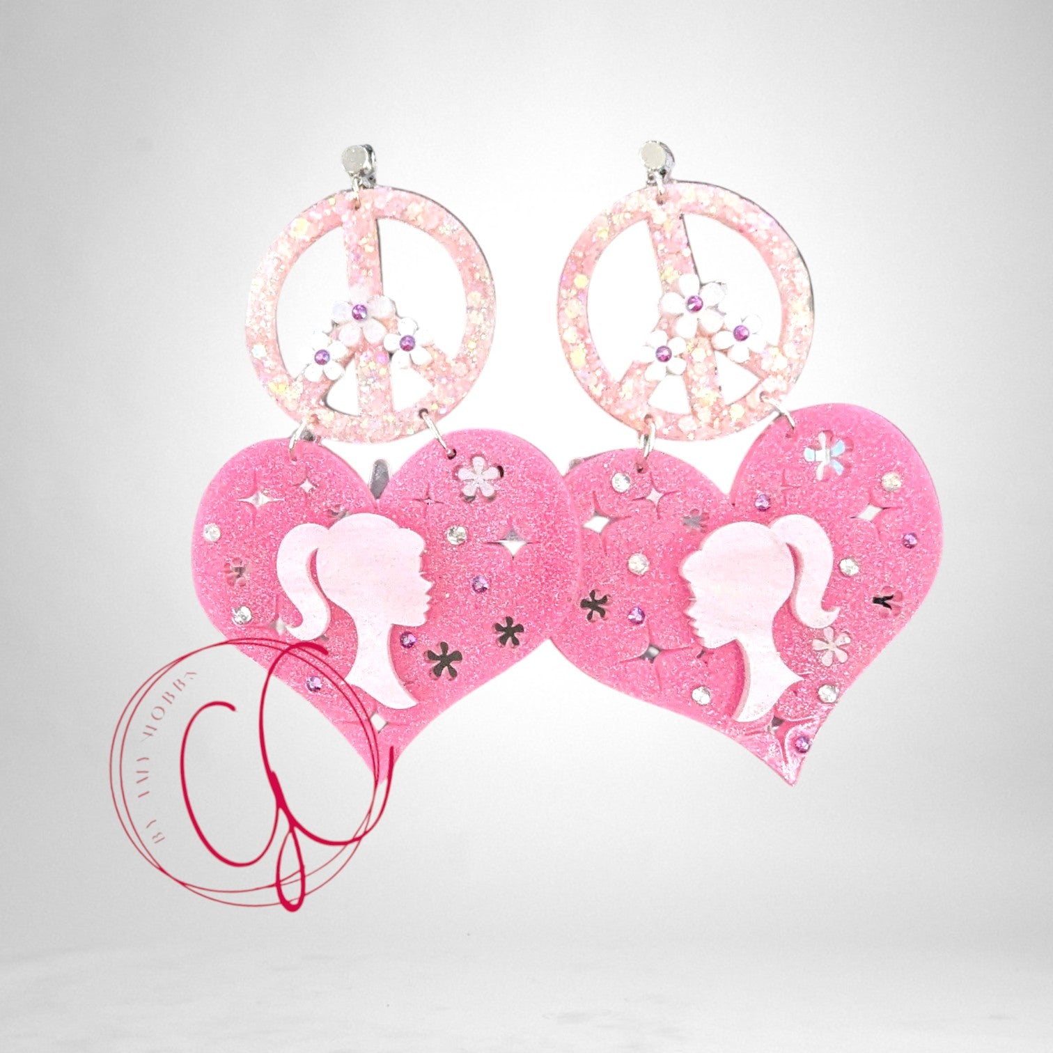 12th Ave Design Co. custom pink glitter heart and peace sign earrings featuring doll silhouettes and floral accents.