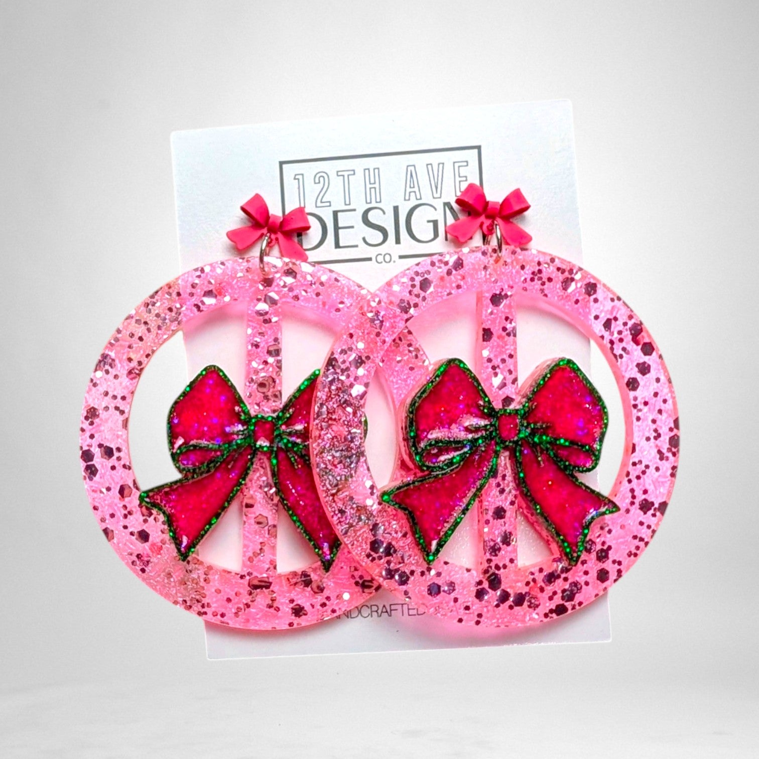 12th Ave Design Co. custom pink glitter resin peace sign earrings featuring festive green-trimmed bows