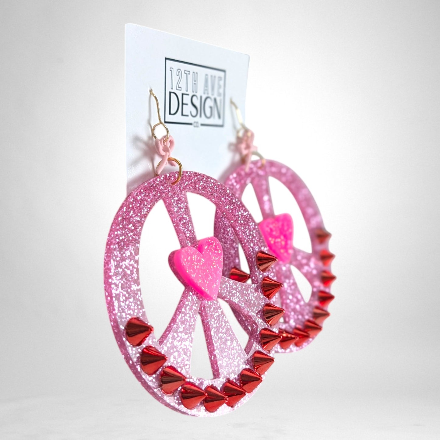 12th Ave Design Co. custom pink glitter peace sign earrings with red spike studs and a central heart accent