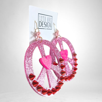 12th Ave Design Co. custom pink glitter peace sign earrings with red spike studs and a central heart accent