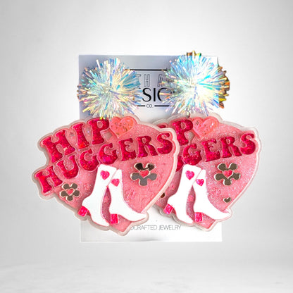 12th Ave Design Co. custom pink heart-shaped resin earrings featuring white cowboy boots and iridescent pom-poms.