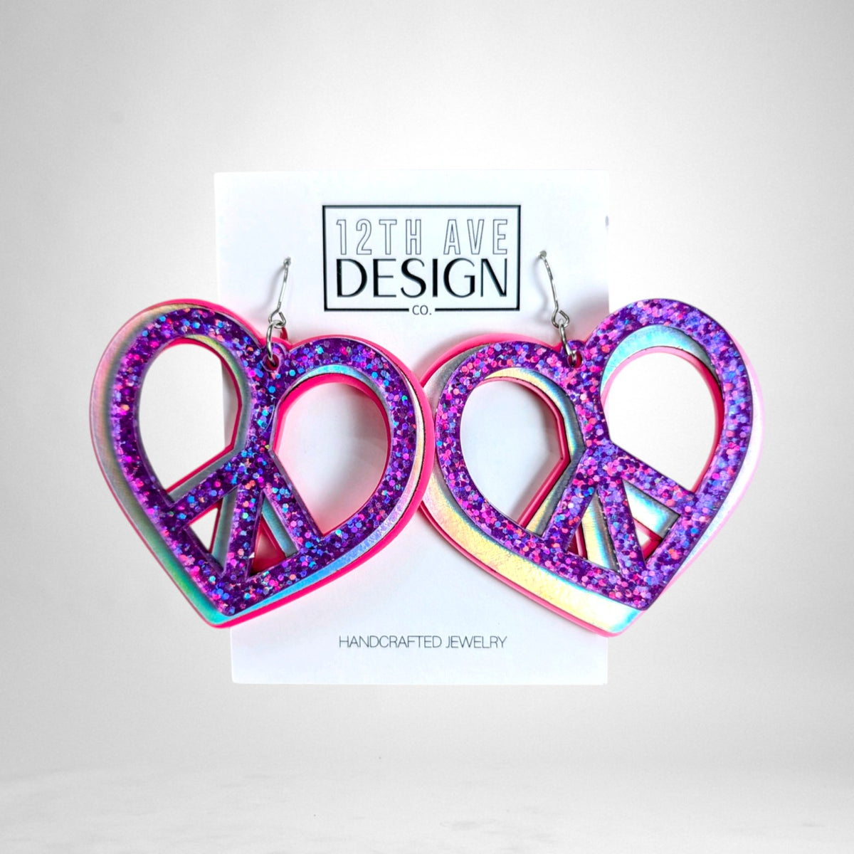 12th Ave Design Co. custom heart-shaped peace sign earrings featuring purple glitter and iridescent acrylic layers.
