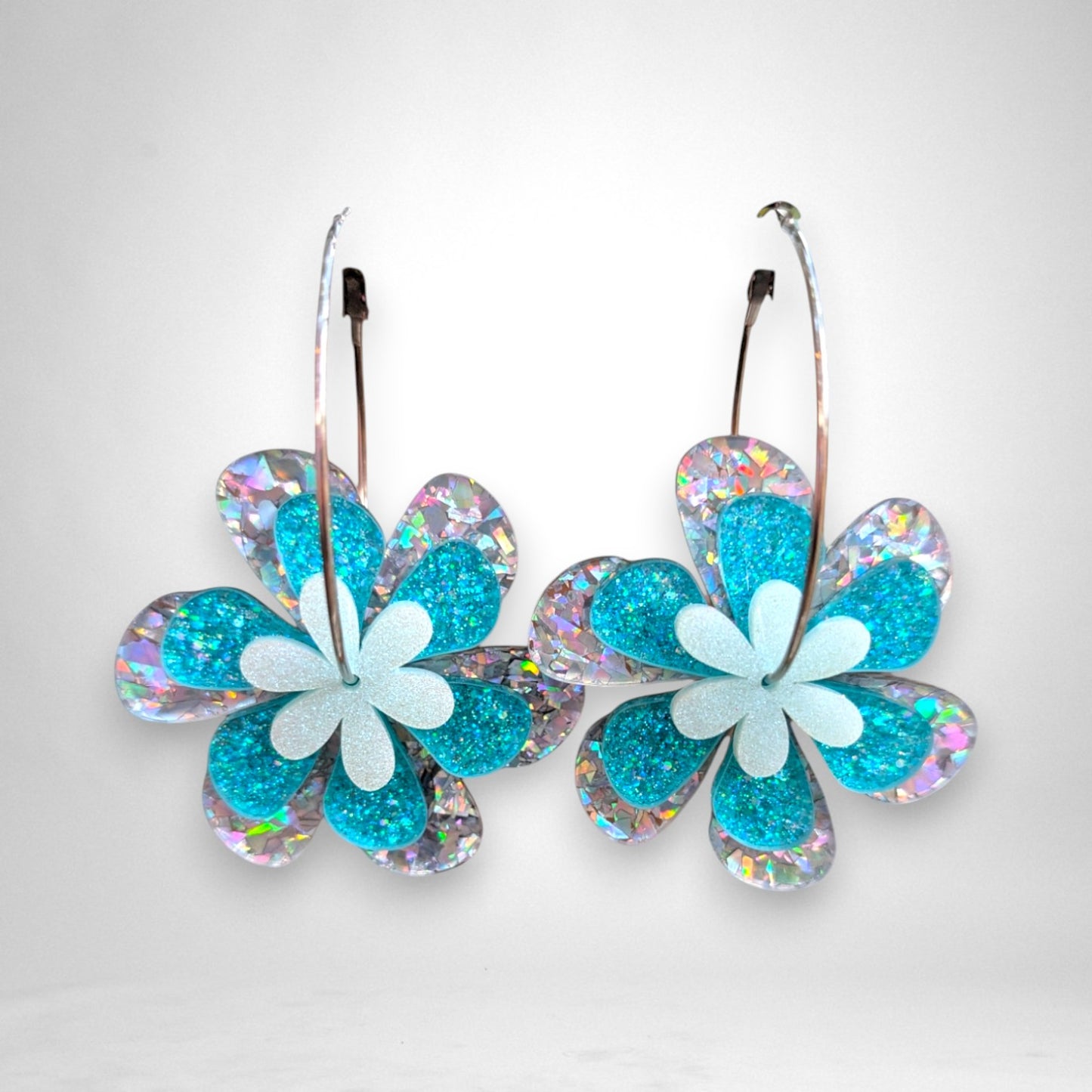 12th Ave Design Co. floating daisy hoop earrings featuring layered teal glitter and iridescent acrylic flowers.