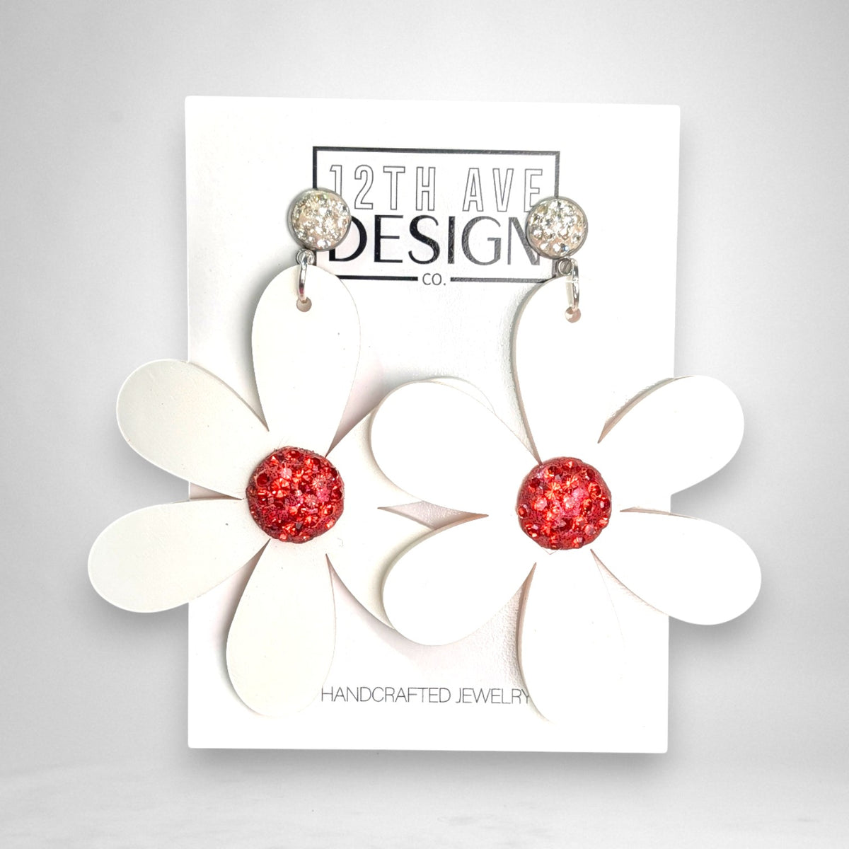 12th Ave Design Co. statement floral earrings featuring white acrylic petals and a sparkling red crystal center.