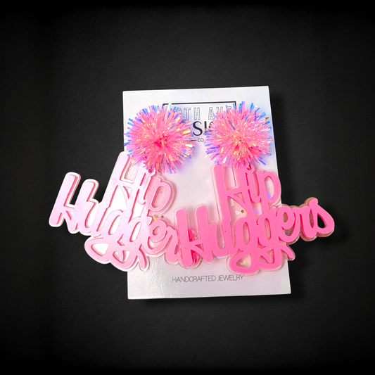 Pink 'Hugger' jewelry with colorful pom-poms on a black background